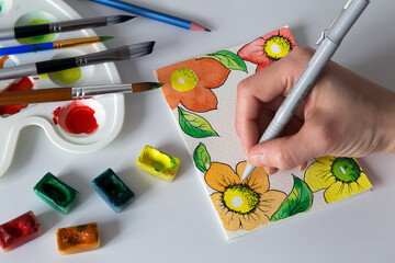handmade postcard with flowers using watercolor paints, brushes and liner, top view