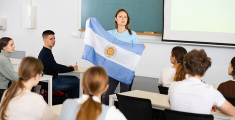 Obraz premium Confident young female professor shows students flag of Argentina