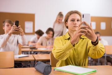 Portrait of schoolgirl using mobile phone while working in classroom during lesson in secondary school