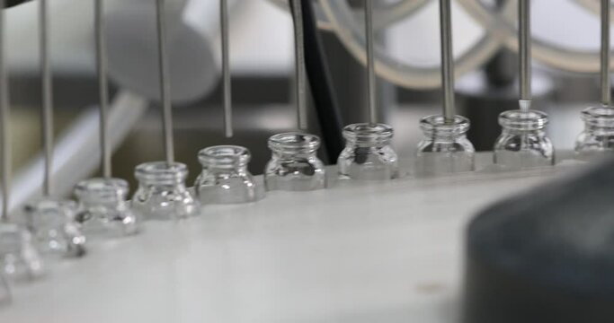 injection filling process in pharmaceutical factory. glass vials in a medicine making factory collected for filling, manufacturing. injection moving in a pharma equipment machinery, vaccine