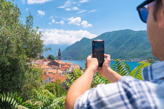 Man tourist taking photo of old town Perast in Kotor bay, Montenegro. Male traveler on summer vacation taking pictures of landmark for social media. Young guy enjoying holidays. Travel destination