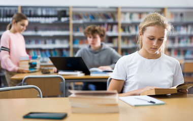 Fototapeta premium Portrait of teenager girl reading books and writing in notebooks in the library
