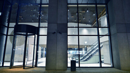 Night view on the ground floor of modern office building with big glass windows and entrance. Street reflection.