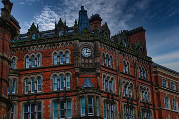 Fototapeta premium Gothic-style red brick building with clock tower under a moody sky in Leeds, UK.