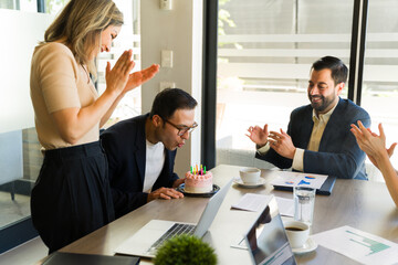 Businessman blowing off the candles of his birthday cake in a meeting room
