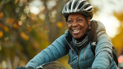 Schilderijen op glas Happy active african american female cycling outdoors in a park. Candid senior lifestyle © Sophie