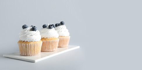 Board of tasty cupcakes with blueberries on grey background