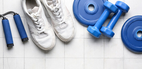 Barbell plates, shoes, skipping rope and dumbbells on white tile background