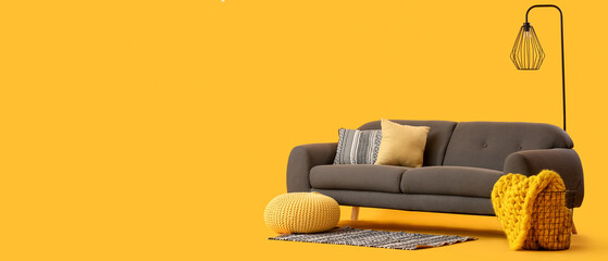 Cozy grey sofa with cushions and pouf on yellow background