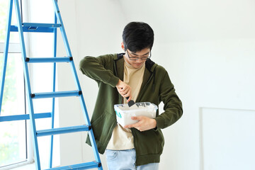 Young Asian man with putty knife and plaster in room