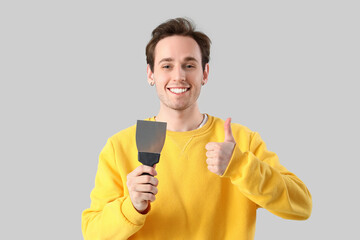 Young man with putty knife showing thumb-up on light background