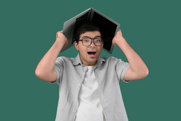 Shocked male programmer with laptop on green background
