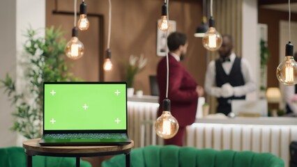 Laptop with blank greenscreen template near hotel reception front desk, people arriving in lobby...