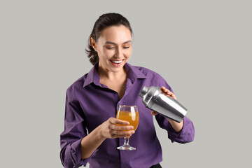 Female bartender with cocktail and shaker on light background