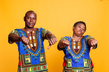 Man and woman showing thumbs down gesture while giving negative review portrait. African american couple posing with dislike sign, showcasing bad feedback and looking at camera
