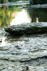 A large stone at the bank of a creek that has an evening sunset reflection shining from the water. 