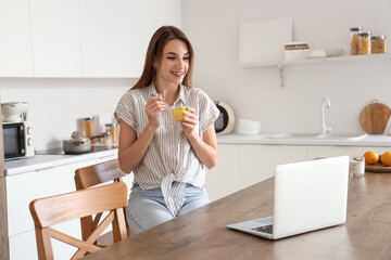 Obraz na płótnie Canvas Young woman with tasty yoghurt and laptop in kitchen