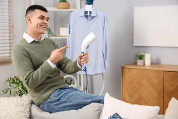 Happy young man with laundry pointing at steamer at home