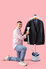Happy young man steaming jacket on pink background