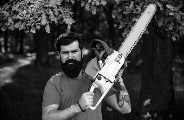 Lumberjack on serious face carries chainsaw. Deforestation is a major cause of land degradation and destabilization of natural ecosystems. Man doing mans job.