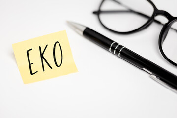 A yellow sticky note on a white background with the handwritten inscription "EKO", next to it a black pen and glasses (selective focus) translation: ECO