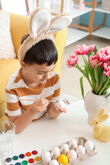 Obraz na płótnie Canvas Cute little boy in bunny ears painting Easter eggs at home
