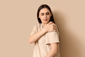 Young woman suffering from shoulder pain on beige background