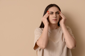 Young woman suffering from headache on beige background