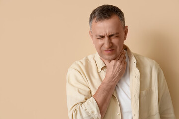 Mature man suffering from sore throat on beige background