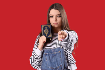 Obraz premium Young woman with Koran pointing at viewer on red background. Accusation concept