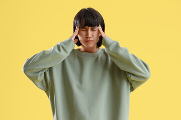 Young woman suffering from headache on yellow background