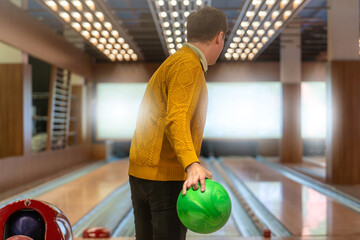 Bowler with green bowling ball ready to take his shot, poised to roll ball down shiny lanes of...