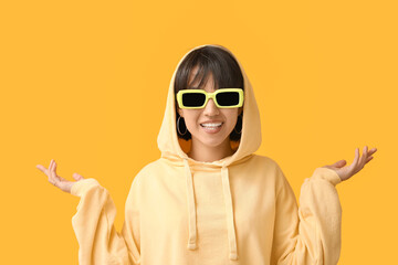 Happy stylish young woman in sunglasses with nose piercing on yellow background