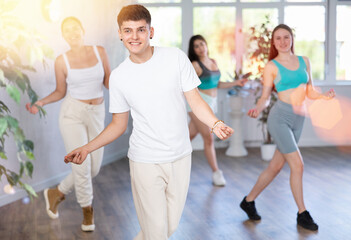 Positive smiling male teenager learns social dance groove, perform movements in choreographic class...