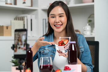 Smiling young beautiful Asian reviewing tasty mixed strawberry and cherry juice detox drinks,...