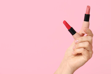 Hand holding lipsticks on pink background