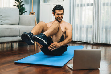 Athletic and sporty man doing crunch on fitness mat while follow online home workout exercise instruction for fit physique and healthy sport lifestyle at home. Online gaiety home exercise video.