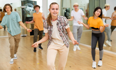 Cheerful teen girl enjoying while training movements of modern group dance in choreography class .