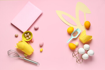 Notepad for recipes with bunny ears, Easter eggs and baking tools on pink background