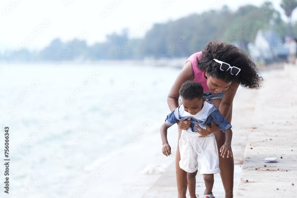 Wall mural Mixed race African and Asian mother and boy is playing at the outdoor area. smiling happy family have fun running on the beach. portrait of mom and kid lifestyle with a unique hairstyle.