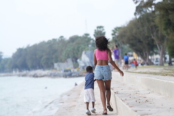 Mixed race African and Asian mother and boy is playing at the outdoor area. smiling happy family have fun running on the beach. portrait of mom and kid lifestyle with a unique hairstyle.