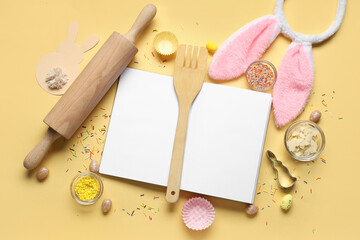 Fototapeta na wymiar Blank notepad for recipes with Easter decor, colorful sprinkles and baking tools on yellow background