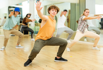 Portrait of cheerful teenage boy practicing hip-hop movements during group dance lesson in studio.