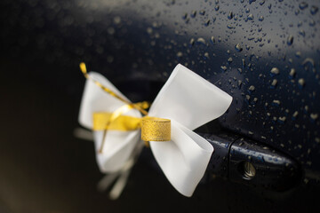 White bow on handle of car door. Rumbling transport to wedding. Bow made of fabric.