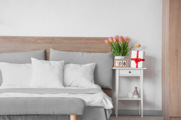 Calendar with date of International Women's Day, tulips and gift box on table in bedroom