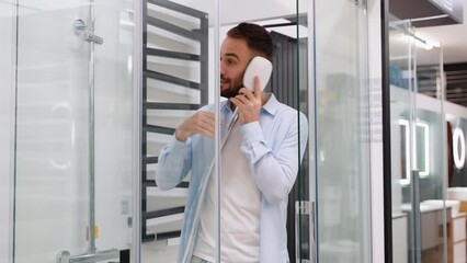 Funny man buyer imitates a phone call in shower cabin in plumbing store