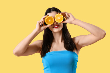 Beautiful young woman in beachwear with oranges on yellow background