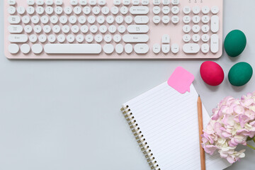 Composition with blank notebook, keyboard, Easter eggs and flowers on grey background