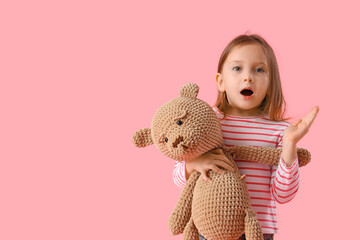 Shocked little girl with teddy bear on pink background