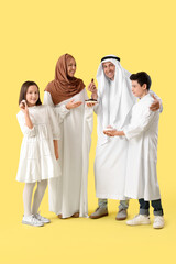 Happy Muslim family with traditional sweets on yellow background. Eid al-Fitr celebration